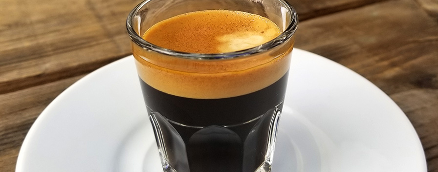 Close up photo of a beautifully dark espresso in a glass cup on a white plate