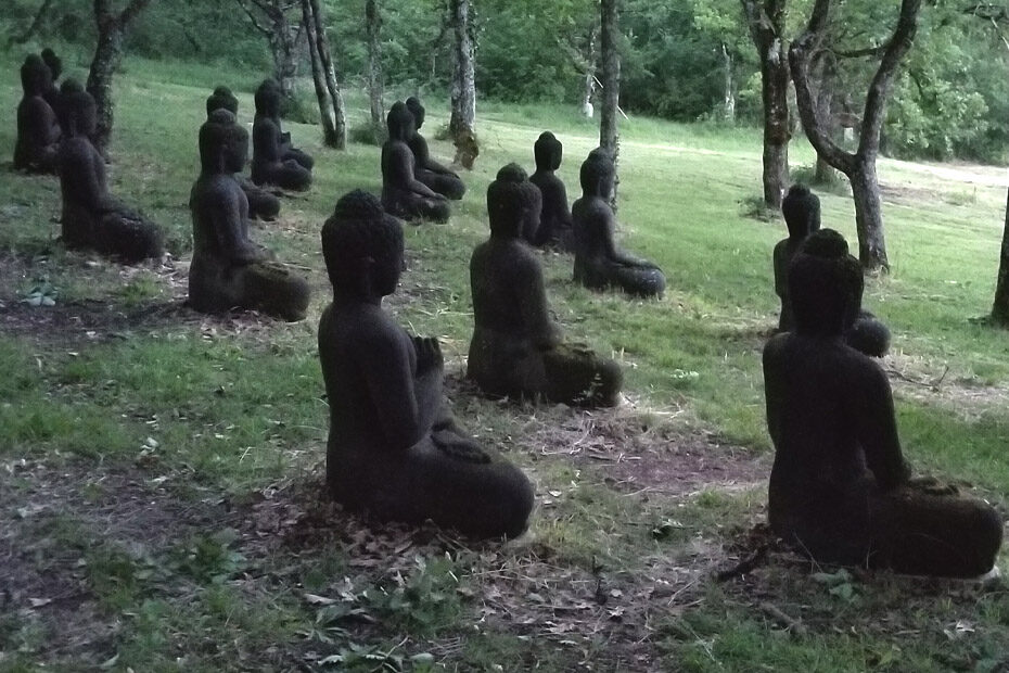 Rows of buddha statues seated in meditation, at Plum Village, France, on a grassy hill, facing out over a field