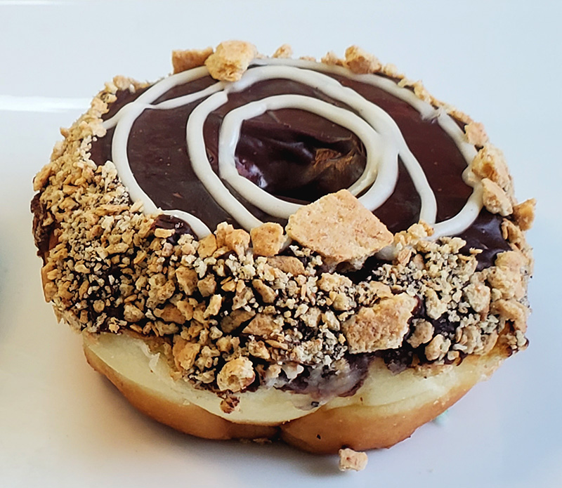 A donut covered in chocolate and swirls of marshmallow icing with graham cracker crumbs around the edge