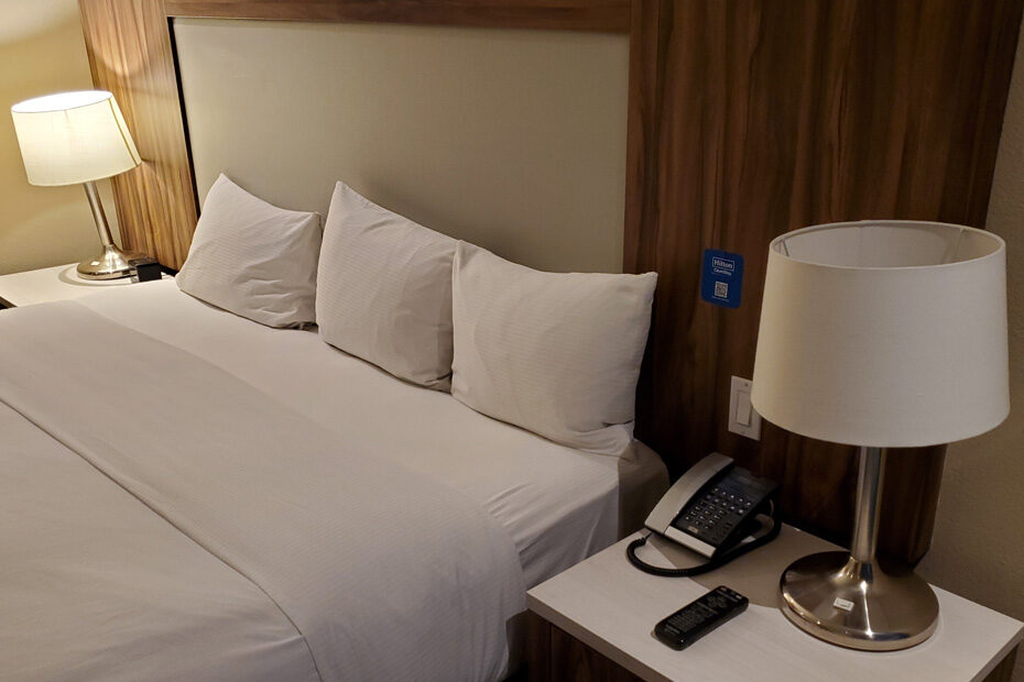 A bed at the Mexico City Airport Hilton. There are plain white sheets and plain white pillows. The pillows are lined up on their sides at the top of the bed, in a row. One pillow is much smaller than the other two in the row.