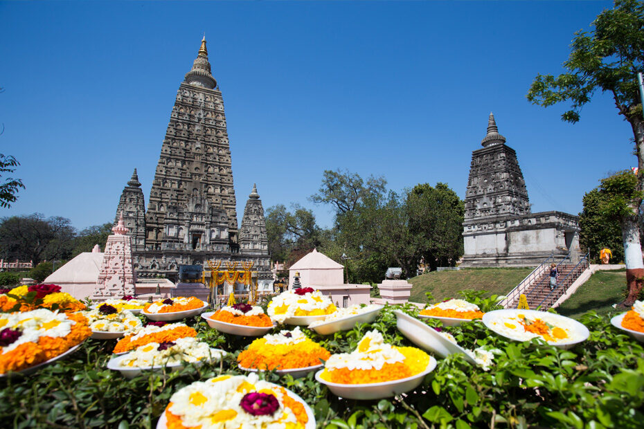 The Mahabodhi Temple, Bodhgaya, India stands tall in the background, with marigolds in bowls resting in the foreground