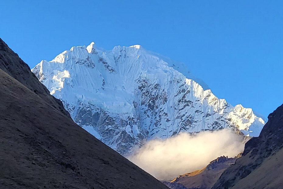 Salkantay Mountain, Peru, covered in snow and ice, still shining in the sunlight against a blue sky, even though its foothills are no dark in shadow