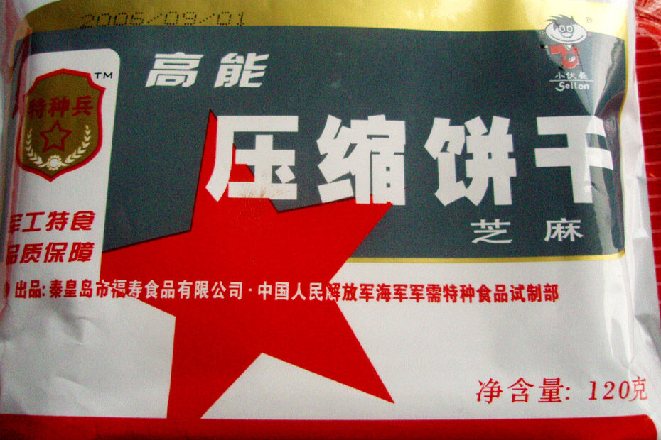 On the train from Beijing, China to Hanoi, Vietnam, a meal replacement bar package. It has a gold strip along the top edge, a red stripe along the bottom, and a red star between the stripes. There is writing in Chinese characters all over it, as well as an official-looking emblem in the top left corner.