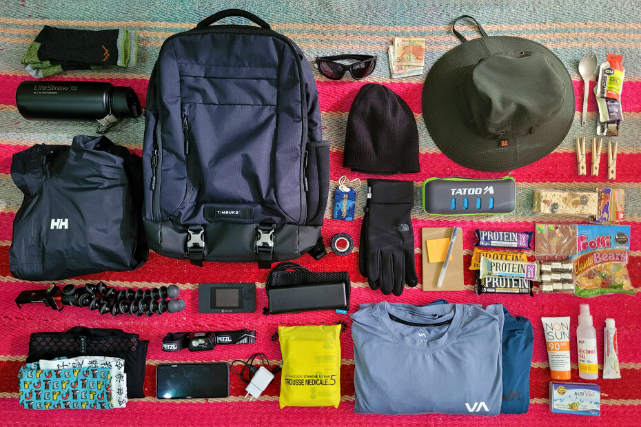 Choquequirao day pack gear laid out on the floor. Hats, portable charger, money, first aid kit, head lamp, candy, tripod, lifestraw thermos, Timbuk2 bag, Darn Tough socks and much more