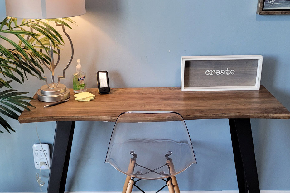 A small desk in an Airbnb with a hard plastic chair and a frame on the desk which has: "create" written inside it in a typewriter font
